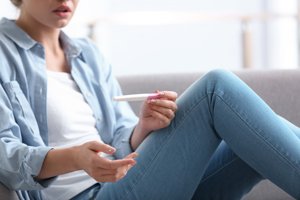 Frau blickt ungläubig auf Schwangerschaftstest