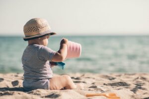 ein baby sitzt am strand und traegt einen sonnenhut