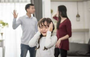 kleines Mädchen weint, während die Eltern im Hintergrund streiten