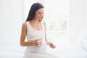 Eine schwangere Frau schaut auf eine Folsäure-Tablette in ihrer Hand