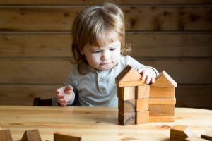 kleines Kind baut Häuser aus Holzbauklötzen
