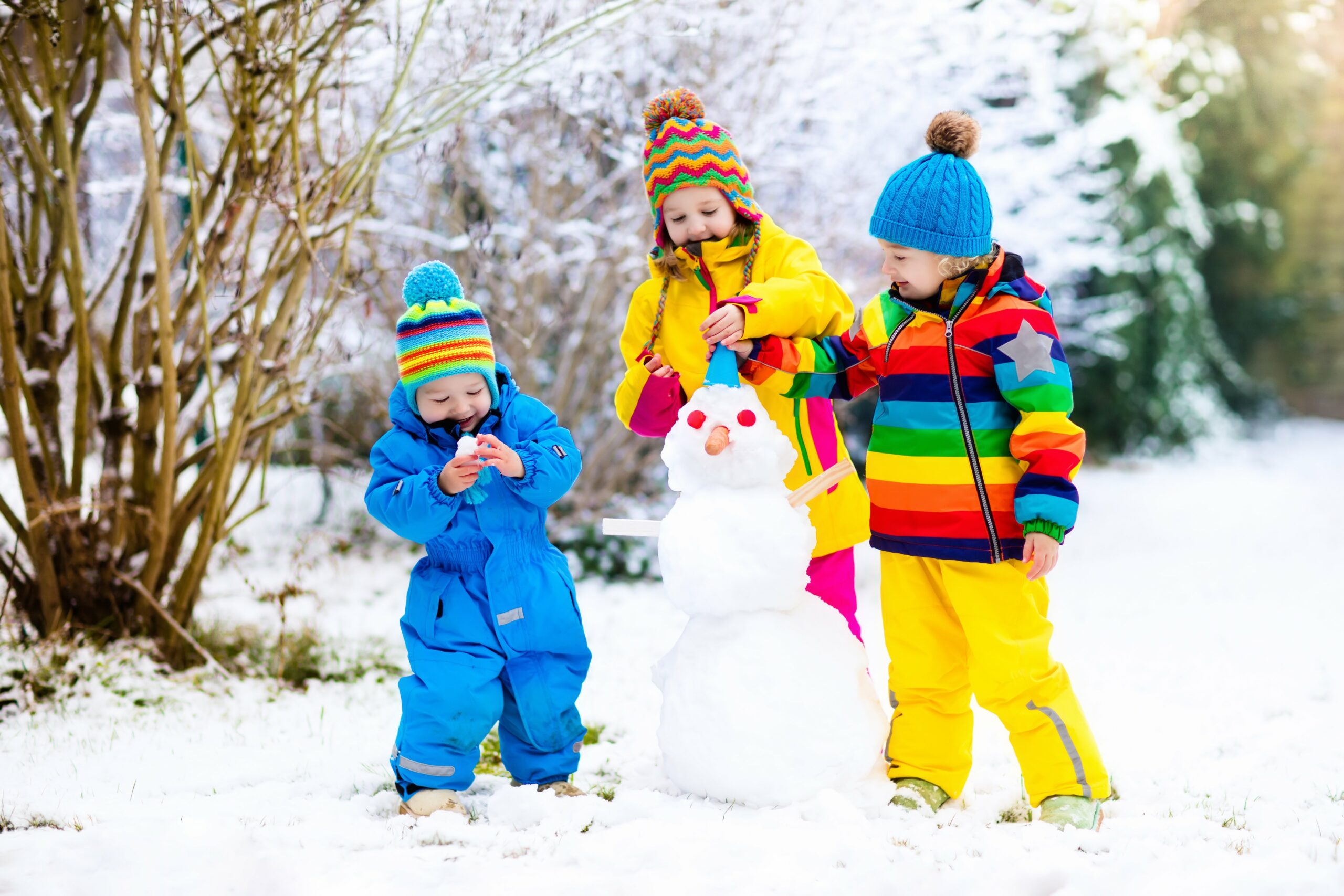 Kinder im Schneeanzug bauen einen Schneemann 