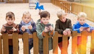 fuenf kinder stehen an einem zaun und schauen auf ihre smartphones
