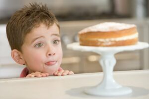 Kind steht mit Appetit vor einem Kuchen