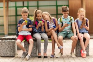 mehrere kinder sitzen mit einem smartphone in der hand nebeneinander