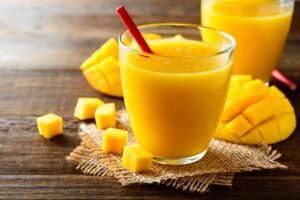 ein mango-smoothie in einem glas mit einer frischen mango auf einem holztisch