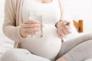 schwangere nimmt eine tablette mit einem glas wasser ein