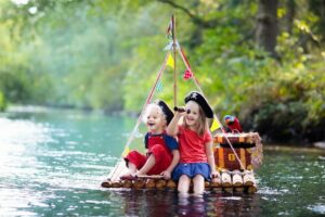 als Piraten verkleidete Kinder fahren auf einem Floß über einen Fluss