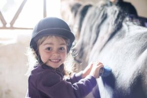 ein kleines Mädchen strigelt ihr Pferd