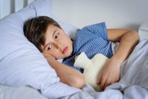 Kind liegt traurig mit Bauchschmerzen im Bett