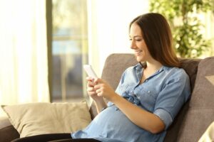 eine schwangere frau mit einem smartphone in der hand