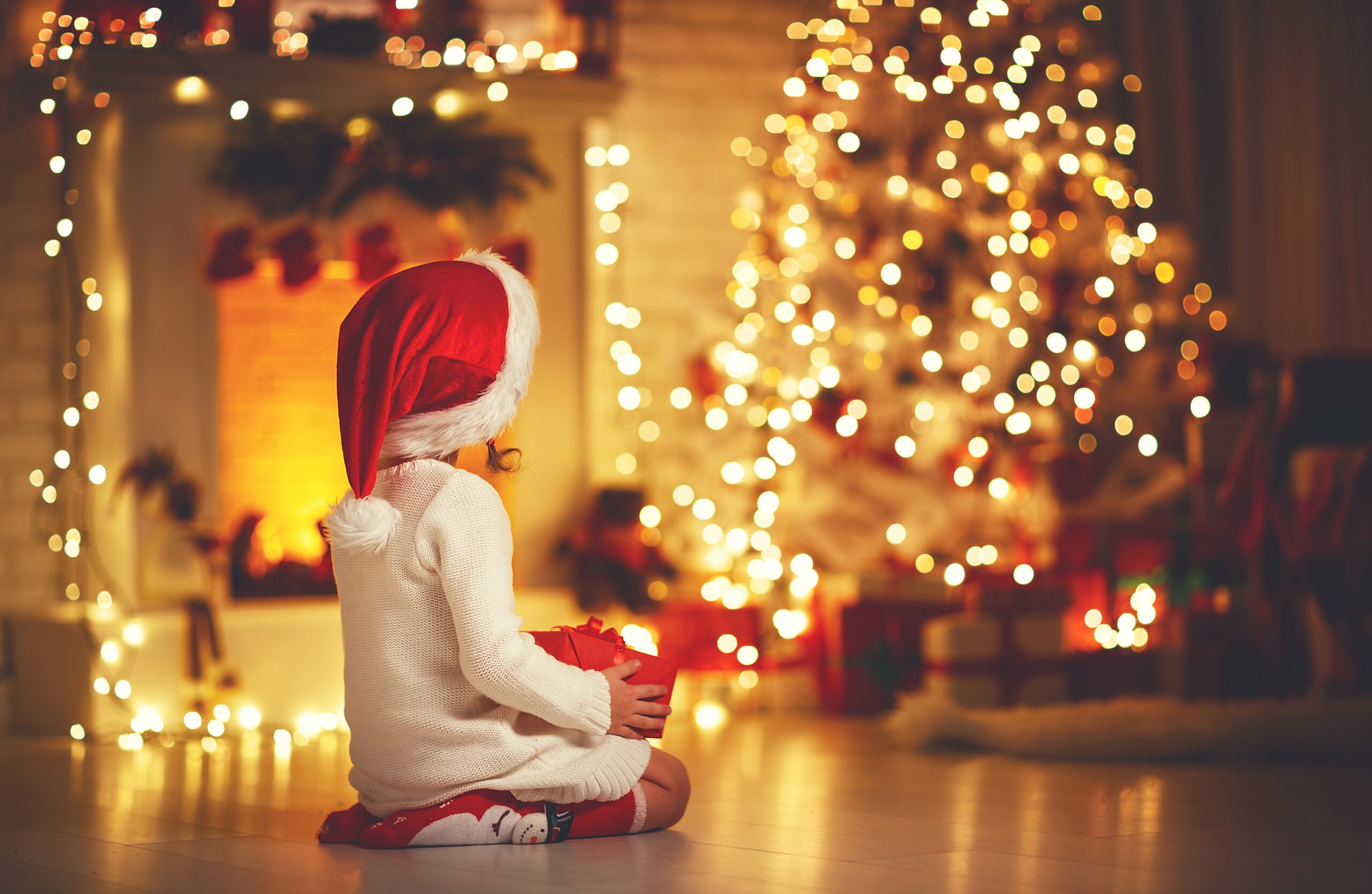 Kleines Mädchen sitzt vor einem Weihnachtsbaum 