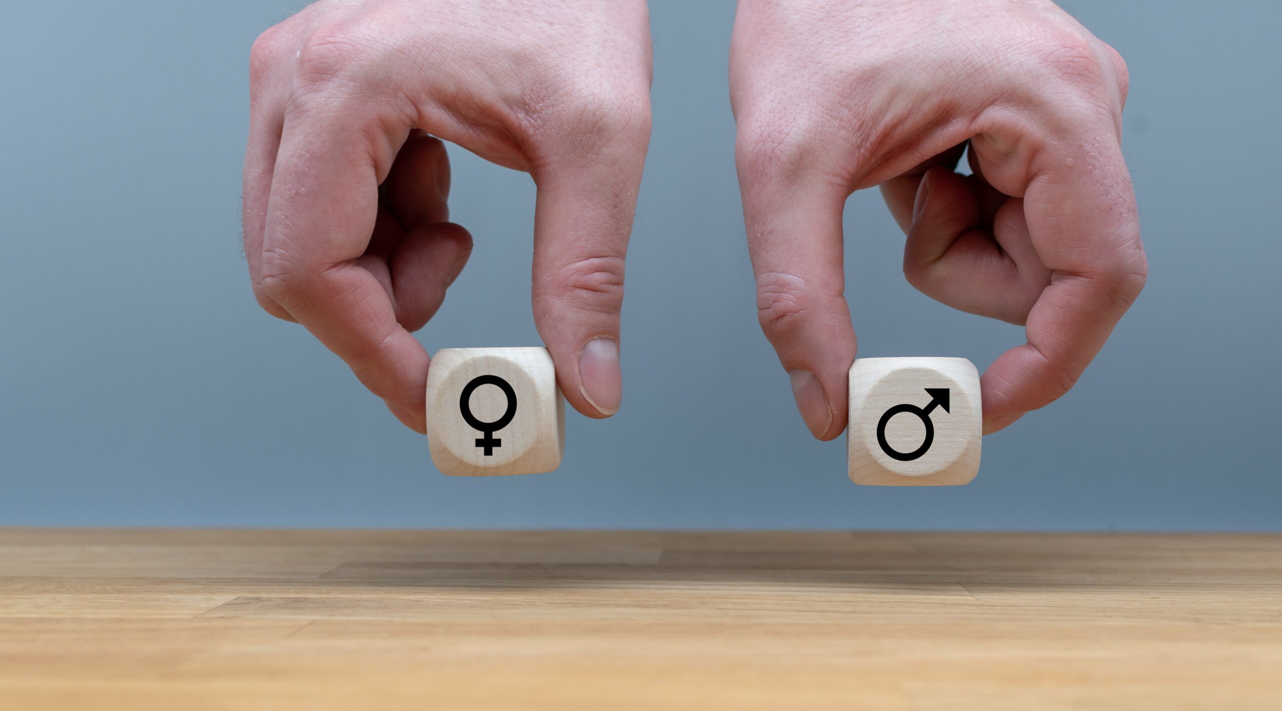 Symbol für Gleichberechtigung zwischen Männern und Frauen. Hände halten zwei Würfel in gleicher Höhe mit den Symbolen für Mann und Frau.